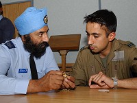Sergeant Balbir Singh Flora, from the RAF Ethnic Minority Recruiting Team, gives trainee fast jet pilot, Flying Officer Jaswant Singh Bhangu, advice on how to modify an RAF cap badge for use on a turban