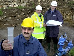 Station Commander RAF St Athan, Wing Commander Sam Ulhaq, inspects a sample of water from the new supply to the Station, while in the background, checking over the plans are, from left,  Mr Clive Francis, DHE Area Manager & Mr Alan Worrall, Atkins Defence.
